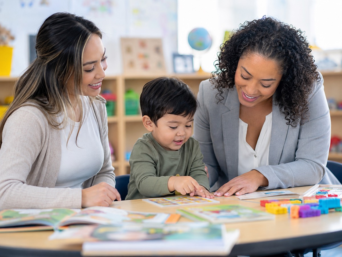 A parent and a specialist looking at picture cards with a toddler at a classroom table